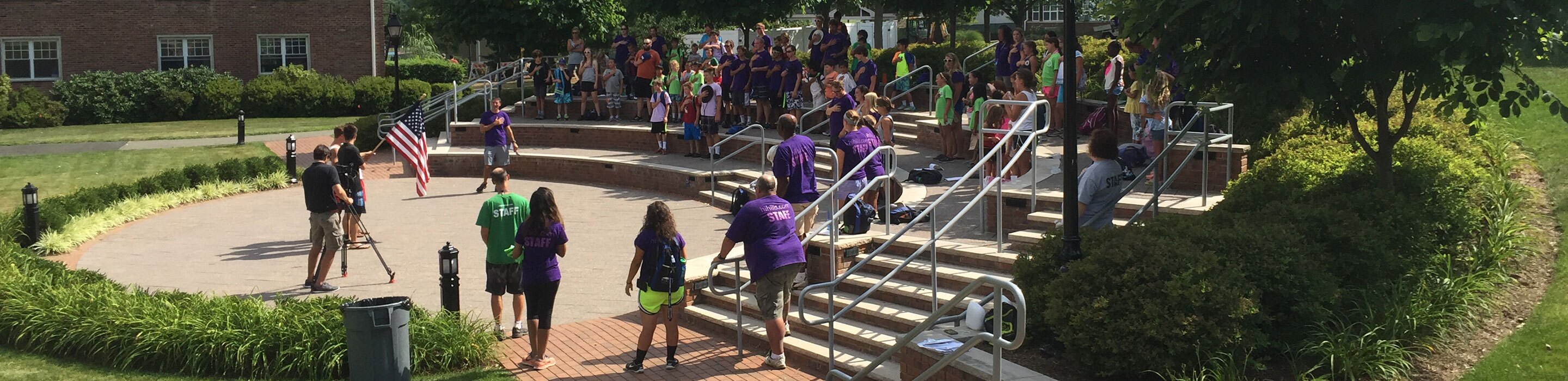 Students and staff are filmed in an outdoor amphitheater for an educational video production