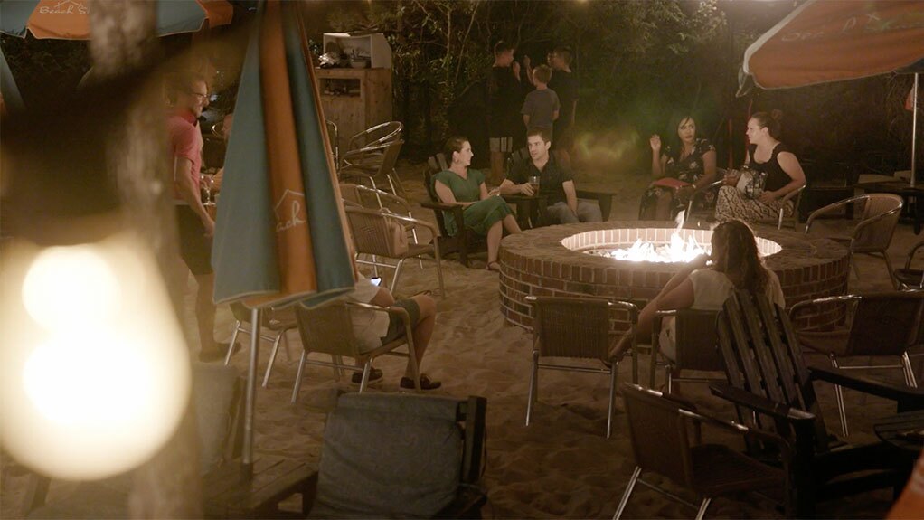 Actors around a firepit having a drink for a commercial video filming.