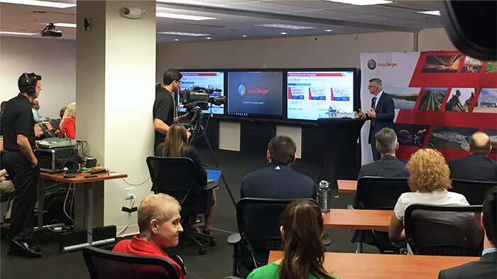 Cameramen and AV crew livestream a corporate video presentation in a large conference room with people
