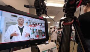 A monitor displays the image of a lab technician