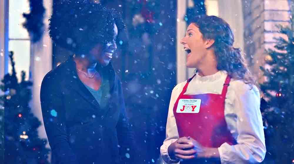 Two female actors smile in the snow fall, during a commercial video production