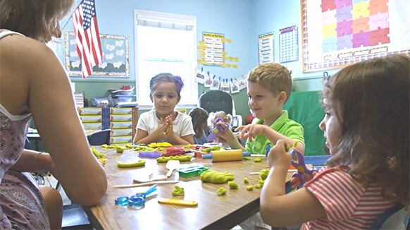 Children and their teacher sitting at a table are filmed for an educational video