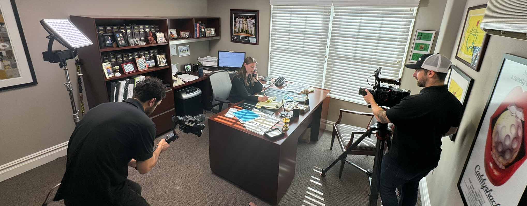 Three crew members prep for a corporate video shoot with a man at a desk