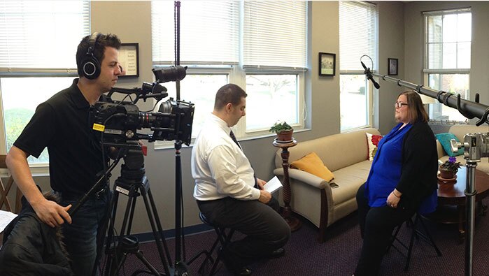 A cameraman, interviewer and staff member are filmed for an education video production