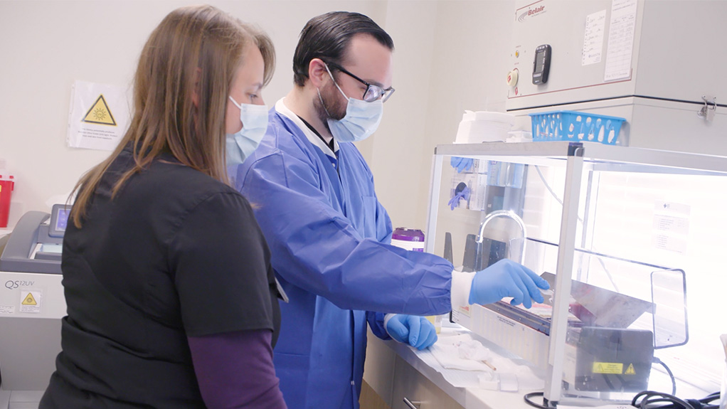 masked lab workers work on a machine in a medical video production