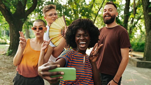 A group of four multiracial friends enjoying their day in a park and making social media posts with a smart phone