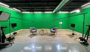 A green screen is setup with cameras lights and chairs, in Awakened Film's Local Studio