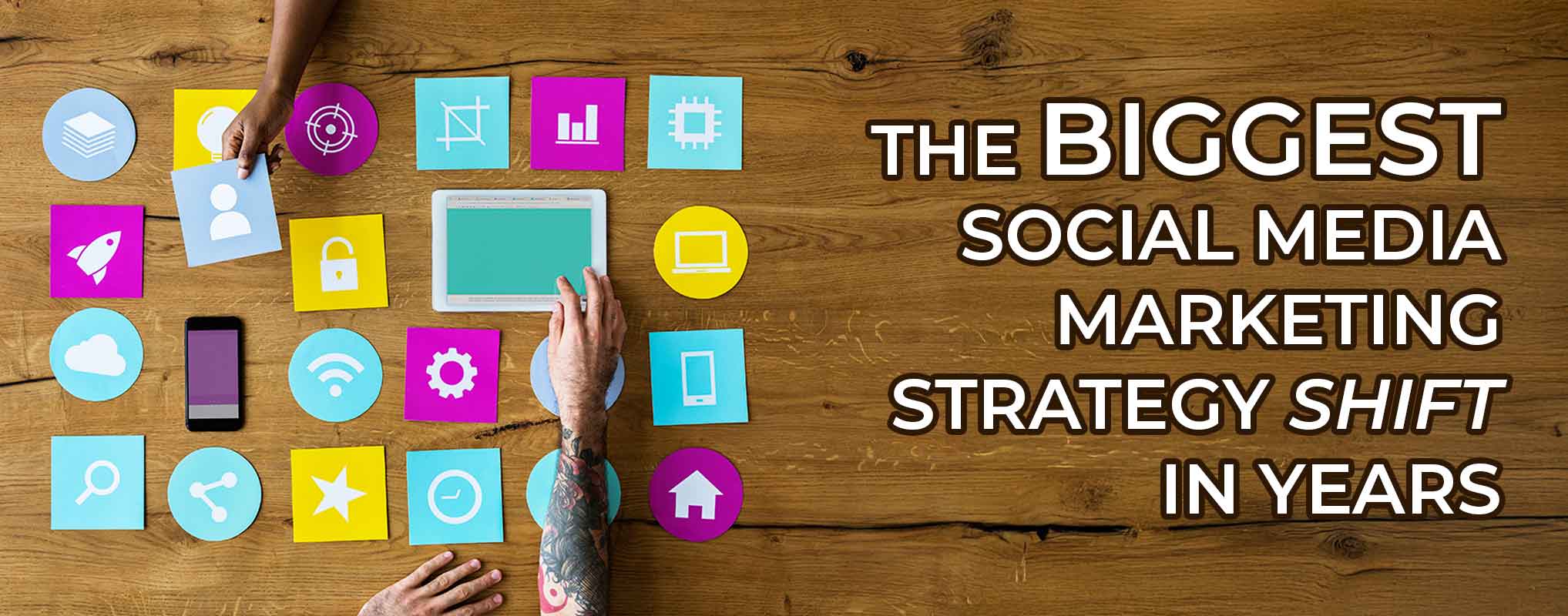 Top down shot of two people moving around social icons on a wooden table, with the words "the biggest social media marketing shift in years"