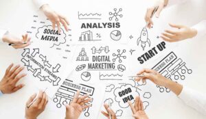 A top down shot of a white table with the words "digital marketing" and a bunch of hands pointing at graphics